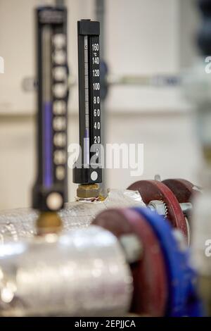 Zentralheizung. Thermometer an der Warmwasserzuleitung zum Heizsystem. Techniker trägt rote Jacke mit weißem Helm. Stockfoto