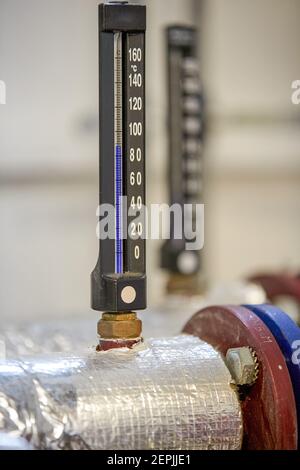 Schwarze Alkoholthermometer, weiße Zahlen, Thermometer und Heizungsrohre. Komponenten der Heiztechnik. Stockfoto