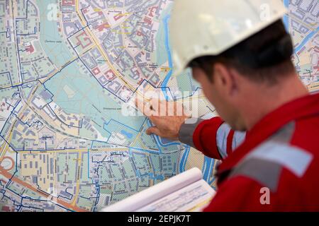 Energiewirtschaft. Ein Techniker mit roten Overalls und einem weißen Helm, der die Heizparameter überprüft. Heizwasserverteilung Technologie.. Stockfoto