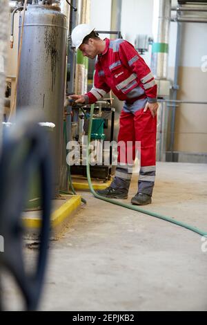 Energiewirtschaft. Ein Techniker mit roten Overalls und einem weißen Helm, der die Heizparameter überprüft. Heizwasserverteilung Technologie.. Stockfoto