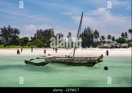 Ein traditionelles Fischerboot aus Mangobaum am Ufer mit Menschen am Strand dahinter, Diani, Kenia, Ostafrika Stockfoto