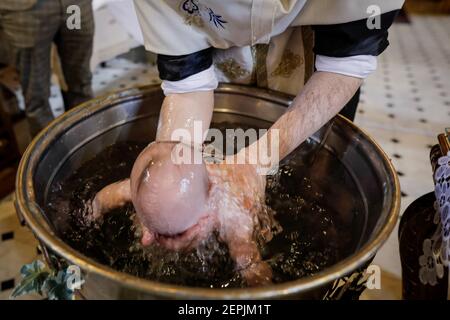 Bukarest, Rumänien - 24. Mai 2020: Details mit einem Baby, das während der Taufzeremonie von einem orthodoxen Priester im Taufbecken versenkt wurde. Stockfoto