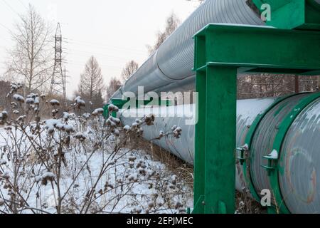 Zentrale Heizrohre in einer schützenden Wärmedämmhülle aus Metall An einem kalten Wintertag über dem Boden gelegt Stockfoto