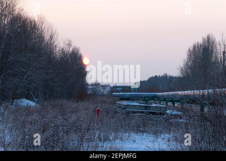 Zentrale Heizrohre in einer schützenden Wärmedämmhülle aus Metall Über dem Boden an einem kalten Winterabend gelegt Sonnenuntergang Stockfoto