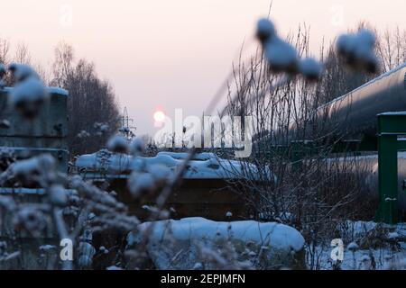 Zentrale Heizrohre in einer schützenden Wärmedämmhülle aus Metall Über dem Boden an einem kalten Winterabend gelegt Sonnenuntergang Stockfoto