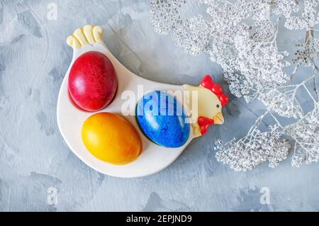 Osterkomposition. Bemalte bunte Eier in einem Keramik-Huhn mit einem Bouquet von frühlingsgelben Mimosen auf dem Ostertisch. Speicherplatz kopieren. Stockfoto