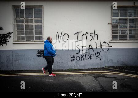 LARNE, NORDIRLAND - Februar, 24 : Ein Mann geht an drohenden loyalistischen Graffiti vorbei, die auf Hafenmitarbeiter in Larne, Nordirland gerichtet sind. Stockfoto