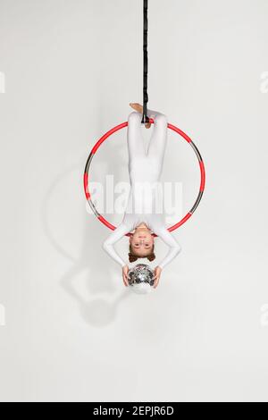 Kleine Mädchen Turnerin in weißer Sportbekleidung zeigt eine akrobatische Performance mit Spiegelkugel auf einem Luftreifen Stockfoto