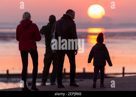 Southend on Sea, Essex, Großbritannien. Februar 2021, 27th. Der warme, sonnige Tag hat mit einem glühenden Sonnenuntergang hinter den Palmen und Besuchern entlang der Küste bei Southend on Sea zu Ende gegangen. Menschen, die auf der Promenade der Western Esplanade spazieren und sitzen, während die Sonne während der COVID 19-Sperre untergeht. Familie für einen Abendspaziergang Stockfoto