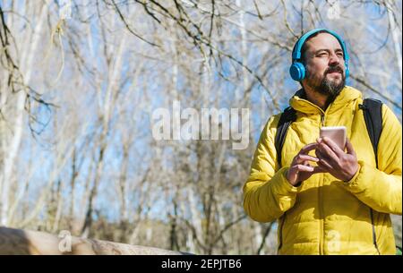 Hipster Mann mit einem Bart Musik hören mit Kopfhörer und Handy, während zu Fuß an einem sonnigen Tag. Stockfoto