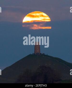 Glastonbury, Somerset, Großbritannien. 27th. Februar 2021. Wetter in Großbritannien. Der Vollschneemon steigt bei Sonnenuntergang hinter einer Wolkenschicht am Glastonbury Tor in Somerset auf. Bild: Graham Hunt/Alamy Live News Stockfoto