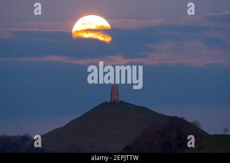 Glastonbury, Somerset, Großbritannien. 27th. Februar 2021. Wetter in Großbritannien. Der Vollschneemon steigt bei Sonnenuntergang hinter einer Wolkenschicht am Glastonbury Tor in Somerset auf. Bild: Graham Hunt/Alamy Live News Stockfoto