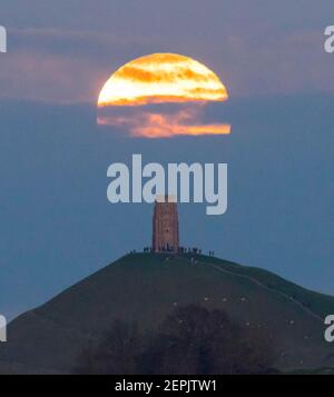 Glastonbury, Somerset, Großbritannien. 27th. Februar 2021. Wetter in Großbritannien. Der Vollschneemon steigt bei Sonnenuntergang hinter einer Wolkenschicht am Glastonbury Tor in Somerset auf. Bild: Graham Hunt/Alamy Live News Stockfoto