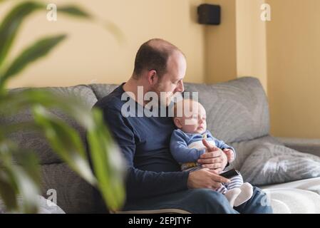 Das häusliche Leben des Vaters in Vaterschaftsurlaub. Vater und Sohn Fußball im Fernsehen zu Hause. Zu Hause in Zeiten der Pandemie Stockfoto