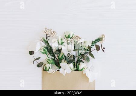 Stilvolle Rosen, Hortensien und Eukalyptuszweige wachsen aus Handwerk Umschlag auf weißem Holz, flach legen mit Kopie Raum. Blumen Grußkarte und Blume Stockfoto