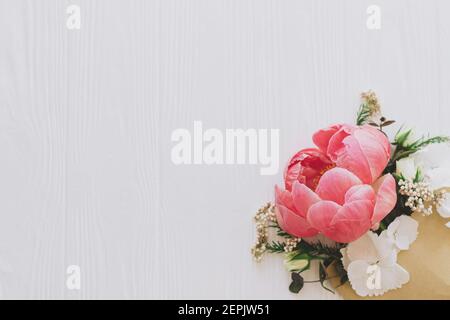 Pfingstrose, weiße Blumen und Eukalyptus wachsen aus Bastelhülle auf weißem Holz mit Platz für Text. Glücklicher Muttertag und Valentinstag. Kreativer Flor Stockfoto