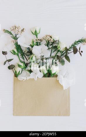 Frühlingsblumen in Umschlag flach legen. Stilvolle Rosen, Hortensien und Eukalyptuszweige und Blütenblätter blühen aus handgefertigte Umschlag auf weißem Holz. Hallo sp Stockfoto