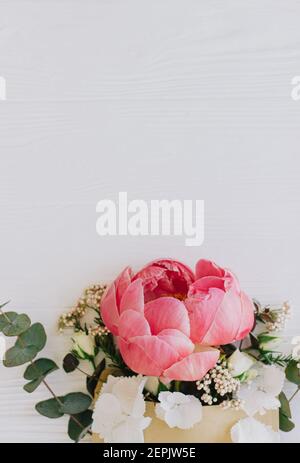 Pfingstrose, weiße Blumen und Eukalyptus wachsen aus Bastelhülle auf weißem Holz, flache Laie mit Platz für Text. Kreative Blumengrußkarte oder senden Stockfoto