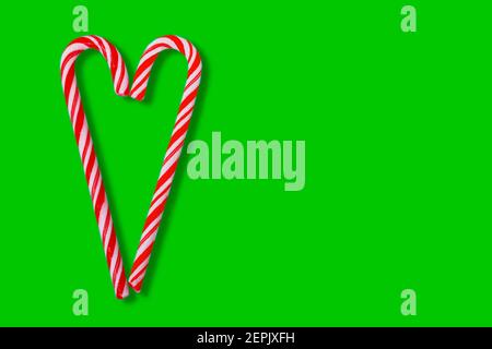 Weihnachtliche Design-Elemen mit zwei rot gestreiften Zuckerrohr in Herz isoliert auf grünem Hintergrund Stockfoto