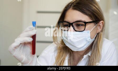 Wissenschaftlerin hält Reagenzglas mit Blutprobe. Das Konzept der Analyse und Diagnostik von Viren und Krankheiten. Stockfoto
