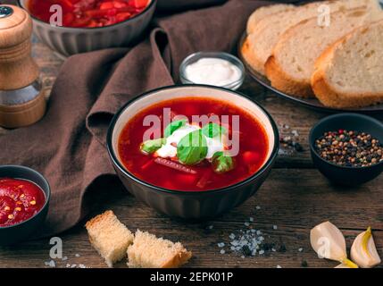 Ukrainischer Borscht in einem Servierteller mit saurer Sahne auf braunem Hintergrund. Stockfoto
