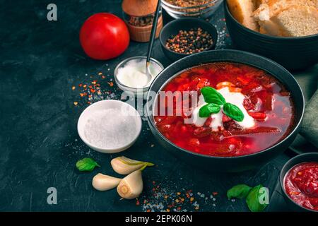 Ein schwarzer Teller mit frischem Borscht auf einem Hintergrund von Zutaten auf einem betonschwarzen Hintergrund. Stockfoto