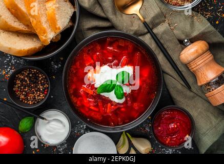 Borscht mit Sauerrahm, Brot und Gewürzen auf schwarzem Hintergrund. Stockfoto