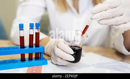 Nahaufnahme einer Pipette, die eine rote Probe in einen Testkolben tropft. Forscherin mit Pipette. Das Konzept der Analysen und Diagnostik Stockfoto