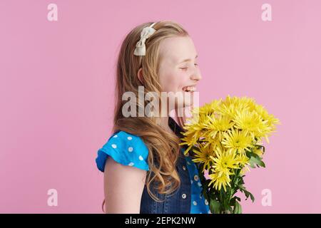 Happy modernes Kind in gepunkteten blau insgesamt mit gelben Chrysanthemen Blumen isoliert auf rosa. Stockfoto