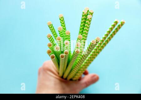 Einwegstrohhalme grün-weiß befinden sich in den Händen gegen ein Blauer Hintergrund Stockfoto