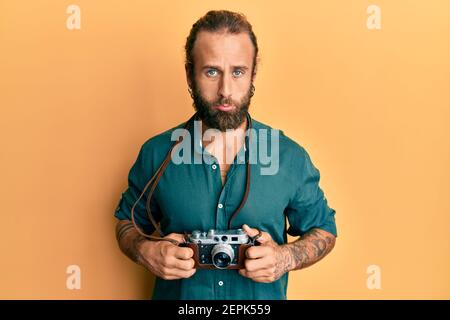 Schöner Mann mit Bart und lange Haare halten vintage Kamera deprimiert und sorgen für Not, Weinen wütend und Angst. Trauriger Ausdruck. Stockfoto