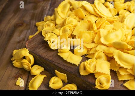 Verschiedene Tartollini mit Käse oder Fleisch zum Kochen in Brühe, verschiedene Formen. Traditionelles Gericht für Feiern in italien, Emilia Romagna Region. Frische hausgemachte Pasta mit Füllung auf einem Holztisch Stockfoto