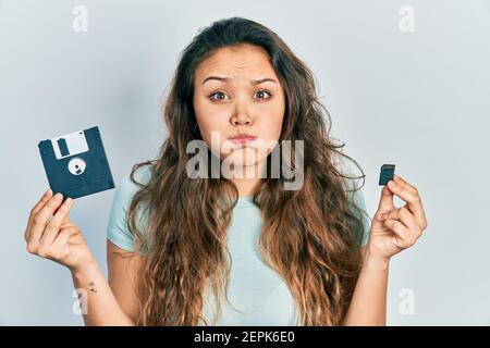 Junge hispanische Mädchen hält Diskette und sdxc-Karte puffing Wangen mit lustigen Gesicht. Mund mit Luft aufgeblasen, Luft fangen. Stockfoto