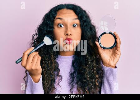 Junge lateinische Frau hält Make-up Pinsel und erröten Puffing Wangen mit lustigen Gesicht. Mund mit Luft aufgeblasen, Luft fangen. Stockfoto