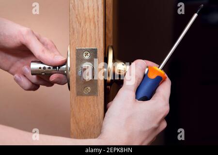 Türinstallation, Arbeiter installiert Türknauf, Holzarbeiter Hände aus der Nähe. Ein Mann dreht den Türgriff mit einem Schraubendreher, repariert den Türgriff mecha Stockfoto