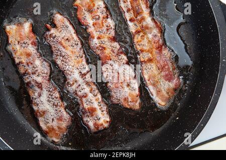 Knusprig rauchiger Speck in Scheiben oder Streifen. Ungesunde fetthaltige Lebensmittel, Mast Zutat. Red dünne Scheibe oder Streifen oder Rasher Speck wird in einer Pfanne gebraten, Schweinefett i Stockfoto