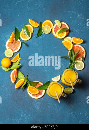Zitrusscheiben - Orange, Zitrone und Grapefruit mit grünen Blättern und Zitrussaft auf blauem Hintergrund, Rahmen, Draufsicht Stockfoto