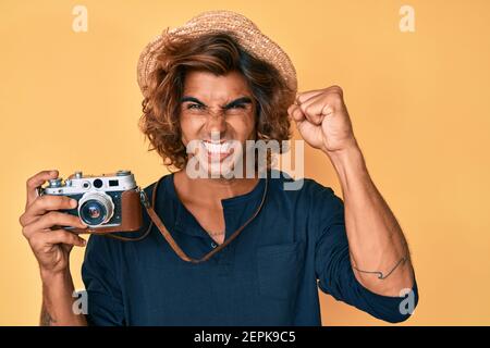 Junger hispanischer Mann mit Hut mit Vintage-Kamera genervt und frustriert schreien vor Wut, schreien verrückt mit Wut und Hand angehoben Stockfoto