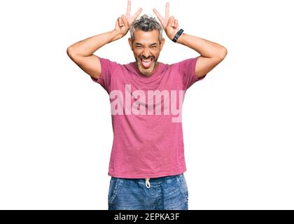 Grauhaariger Mann mittleren Alters in lässiger Kleidung, lustig und verrückt posiert mit Fingern auf dem Kopf als Hasenohren, lächelnd fröhlich Stockfoto