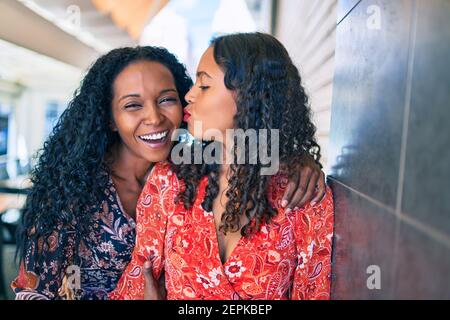 afroamerikanische Mutter und Tochter umarmen und küssen, lehnen an der Wand. Stockfoto