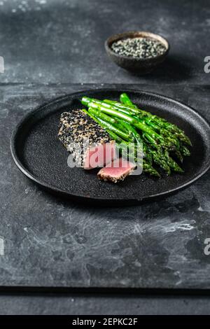 Gebratenes Thunfischsteak in schwarzem Sesam mit Spargel auf Schwarz Platte Stockfoto