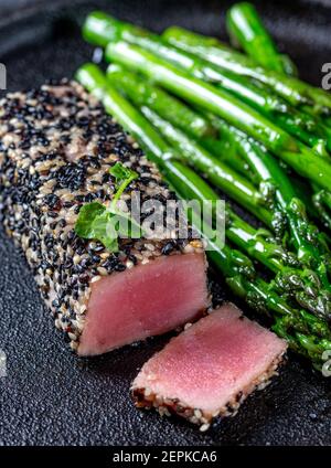 Gebratenes Thunfischsteak in schwarzem Sesam mit Spargel auf Schwarz Platte Stockfoto