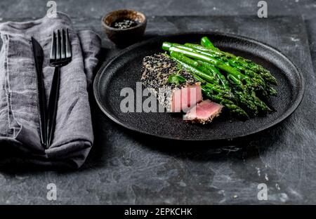 Gebratenes Thunfischsteak in schwarzem Sesam mit Spargel auf Schwarz Platte Stockfoto