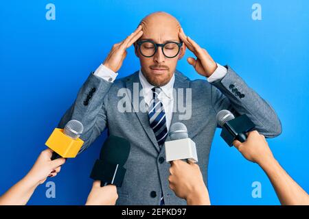 Glatze Mann mit Bart von Reportern interviewt halten Mikrofone mit der Hand auf dem Kopf, Kopfschmerzen, weil Stress. Leiden Migräne. Stockfoto