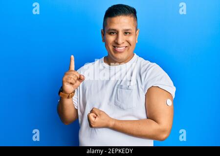 Junger lateinischer Mann mit Glucosemesser Taste lächeln mit einer Idee oder Frage Zeigefinger mit glücklichen Gesicht, Nummer eins Stockfoto