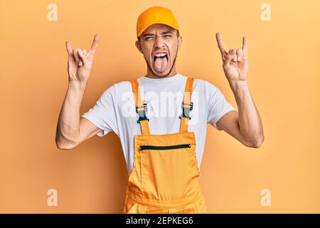 Hispanic junger Mann trägt Handyman Uniform schreien mit verrückten Ausdruck Rock-Symbol mit Händen nach oben. Musik-Star. Heavy-Musik-Konzept. Stockfoto