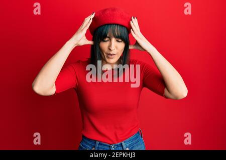 Junge hispanische Frau trägt französisch Look mit Baskenmütze mit Hand auf Kopf für Schmerzen im Kopf, weil Stress. Leiden Migräne. Stockfoto