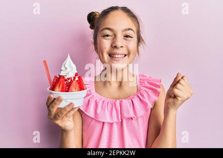 Schöne Brünette kleines Mädchen essen Erdbeere Eis schreien stolz, feiert Sieg und Erfolg sehr aufgeregt mit erhobenem Arm Stockfoto