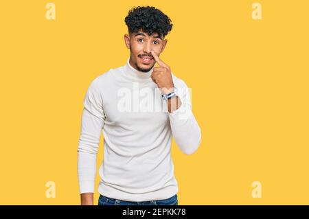 Junger arabischer Mann trägt lässigen Winter Pullover zeigt mit Hand Finger zu Gesicht und Nase, lächelnd fröhlich. Beauty-Konzept Stockfoto