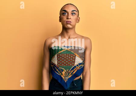 Hispanic Mann trägt Make-up und lange Haare tragen Womans Top Puffing Wangen mit lustigen Gesicht. Mund mit Luft aufgeblasen, verrückte Ausdruck. Stockfoto